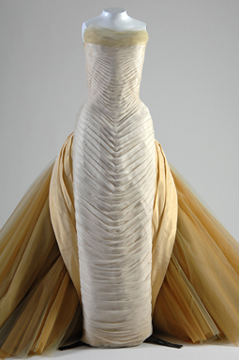 mannequin in a fitted floor-length strapless dress with horizontal pleats and a large tulle train in the back