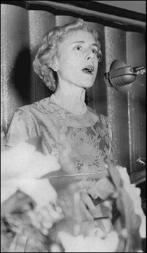 woman with styled blond hair standing at a 1940s microphone