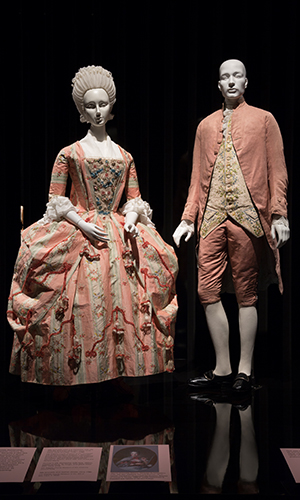 platform view of (left)silk brocade robe à la française with leather shoes and (right) man's silk faille ensemble with brass, silver-plated shoes.